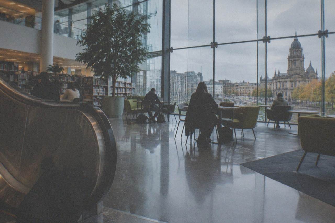 Visitors reading beneath the high ceilings of the Library of Birmingham on a wet afternoon