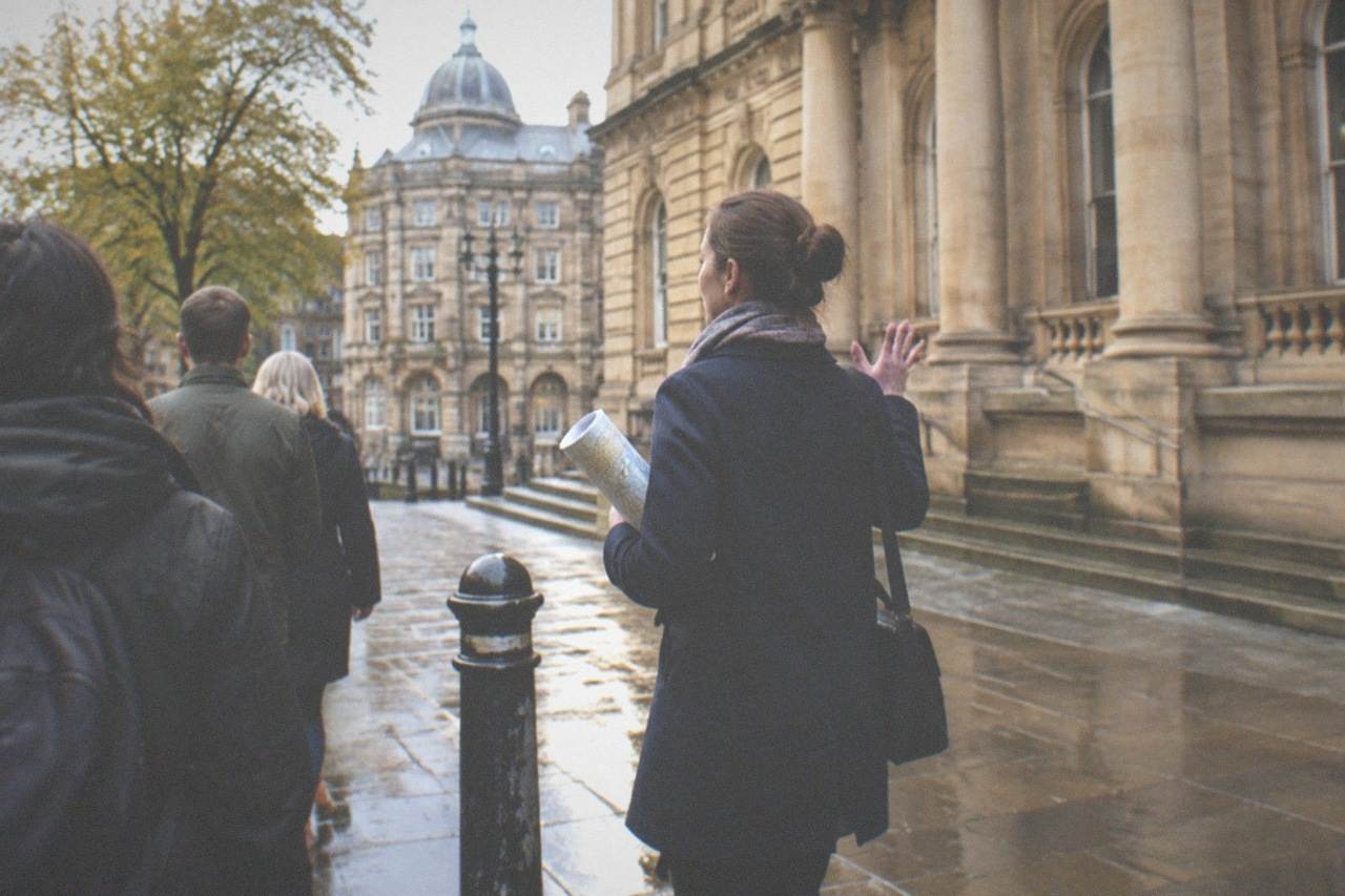A guide gestures toward the Victorian civic buildings of Chamberlain Square while a small free walking-tour group listens in central Birmingham.